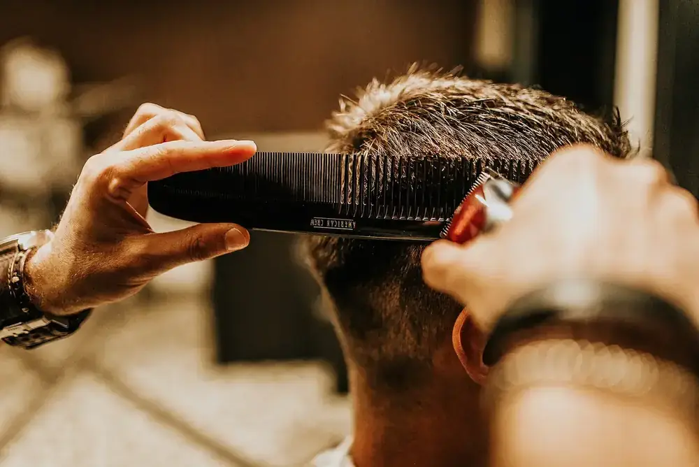 Barbero perfilando el corte de un cliente con peine y máquina